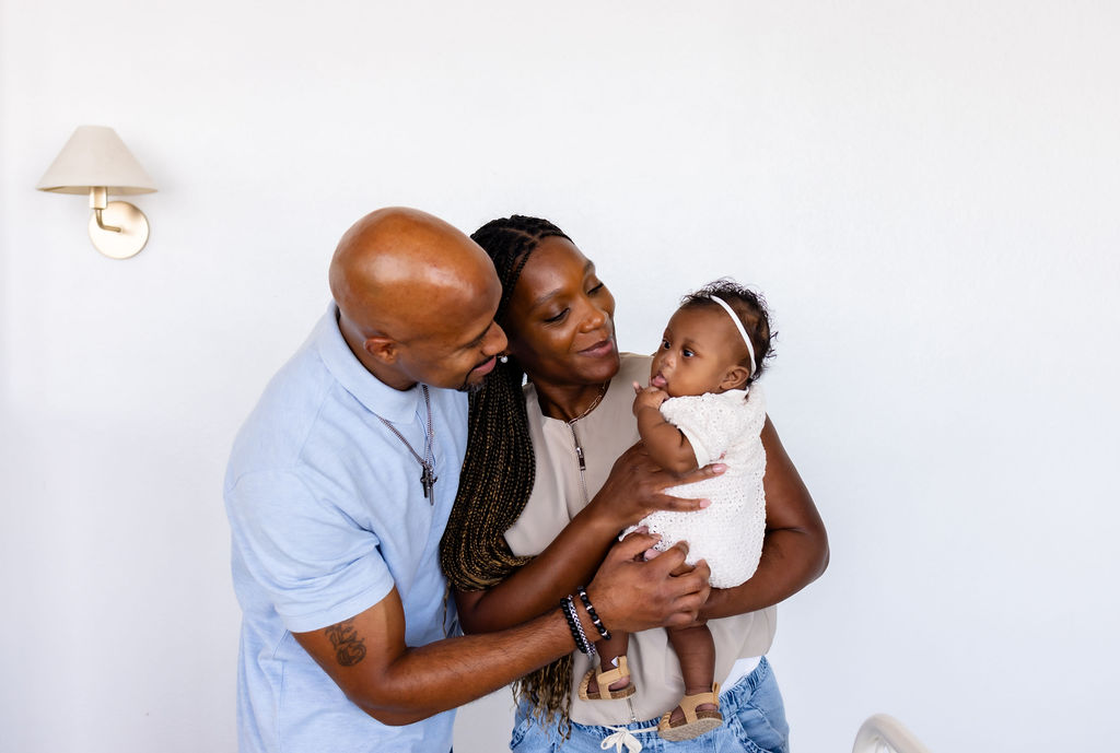 Parents smiling and leaning toward their infant while holding them together
