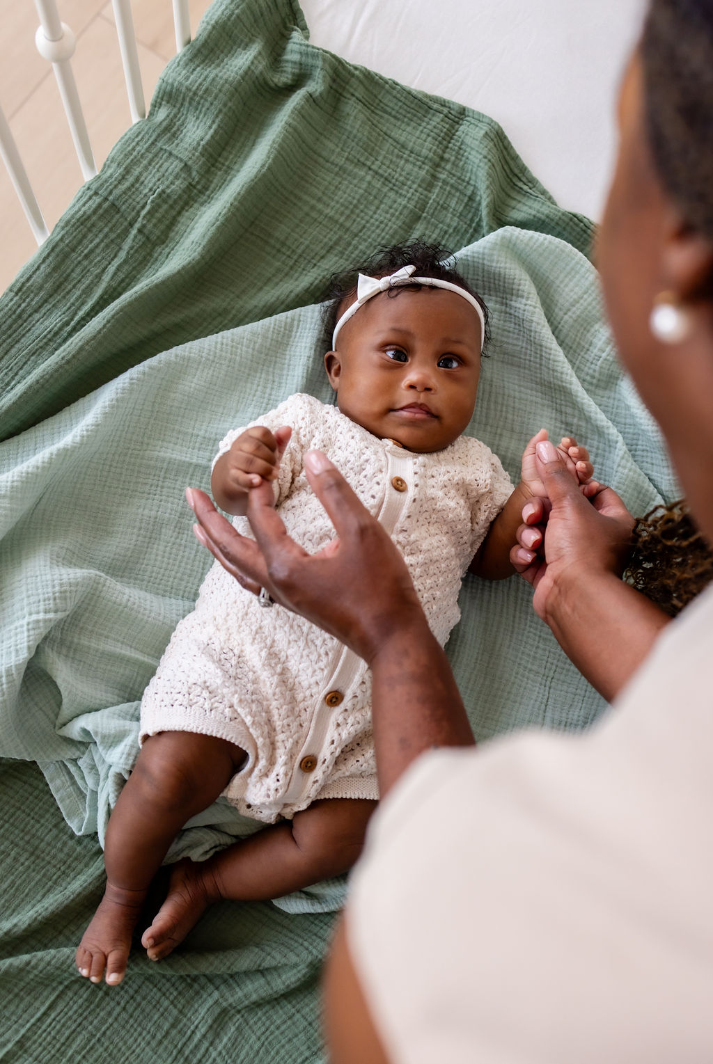 A caregiver holding an awake infant's hands while the infant looks toward her