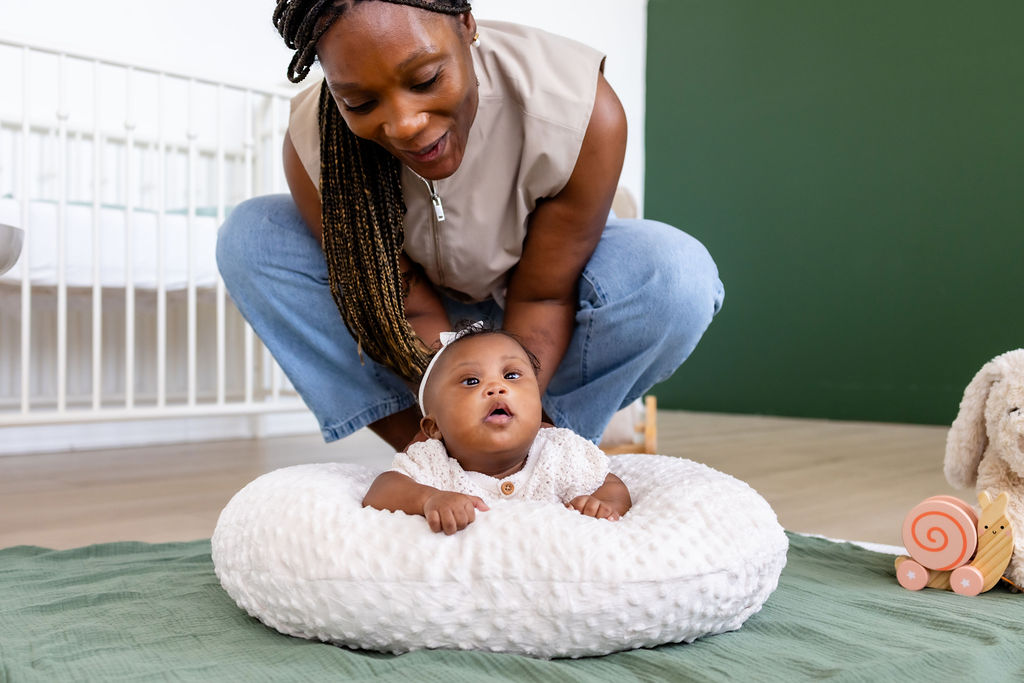 A caregiver supporting her awake infant during tummy time on a white cushion