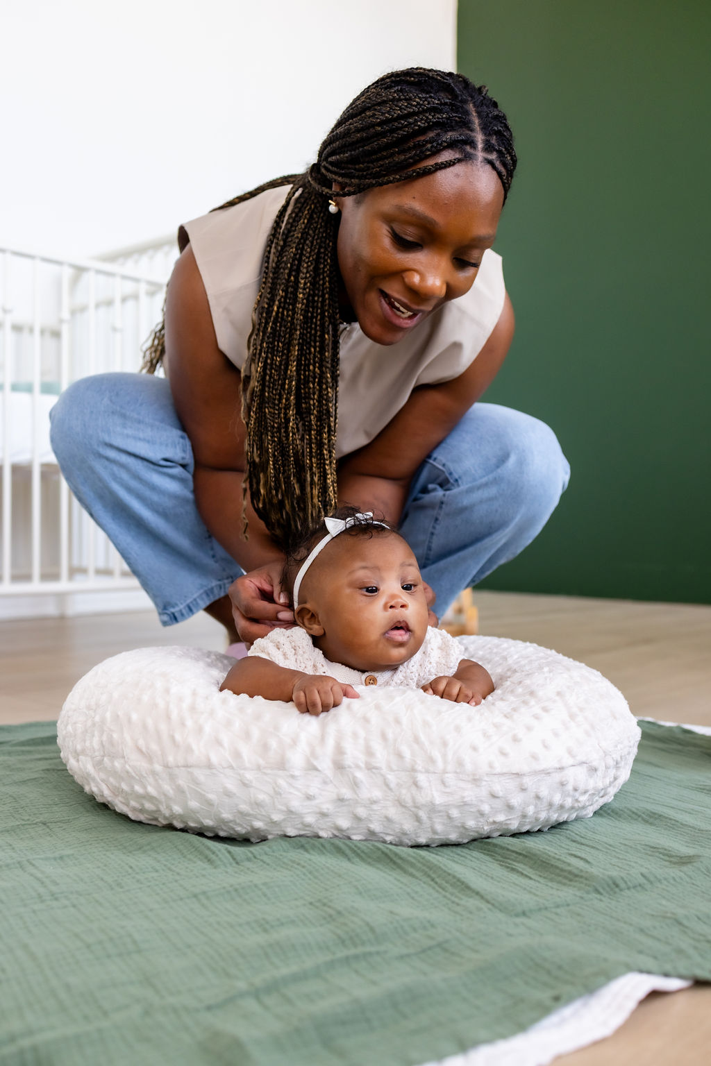 A caregiver supporting her awake infant during tummy time on a white cushion