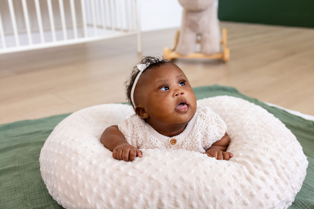 An awake infant looking up during tummy time on a white cushion