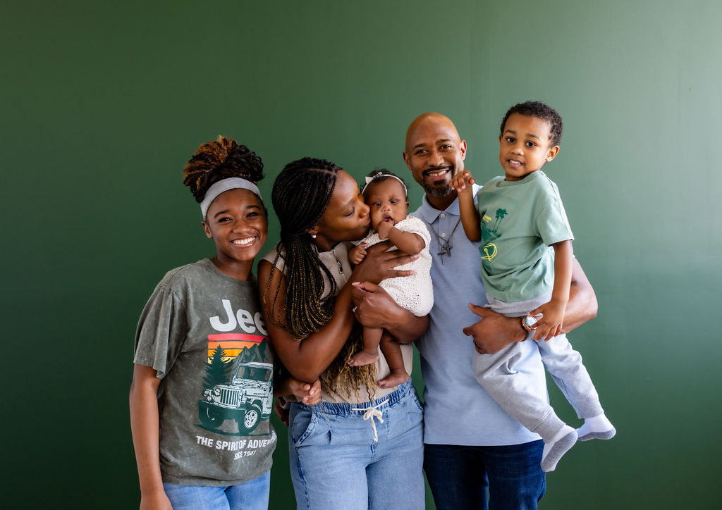 A family with parents, an infant, and older children posing against a green background