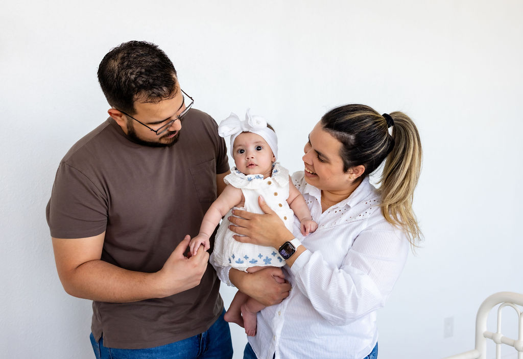 Parents holding their infant beside a white crib