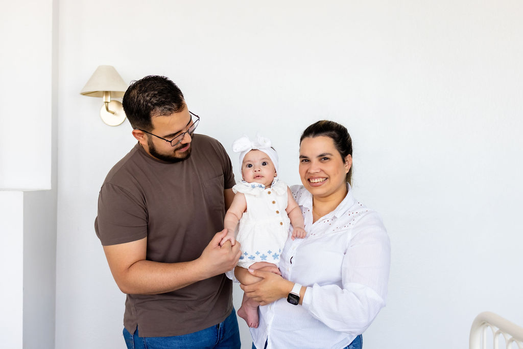 Parents holding their infant beside a white crib