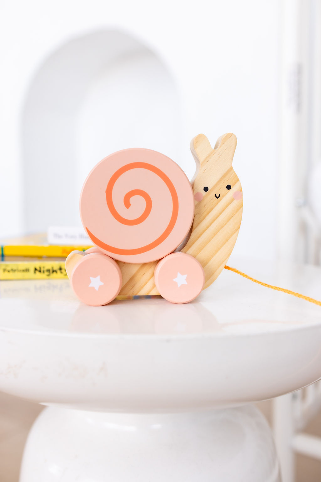 A wooden snail toy and books on a white side table