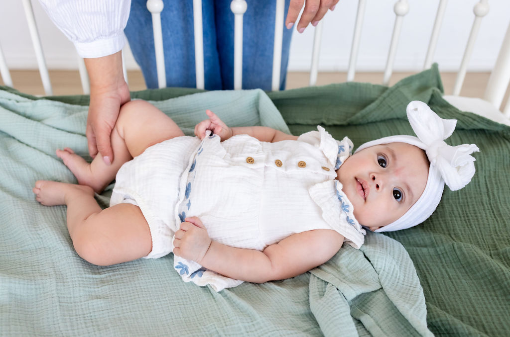 A caregiver touching the legs of an awake infant lying on a green blanket